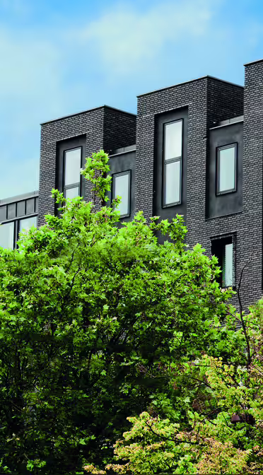 Modernes schwarzes Gebäude mit eleganten, rechteckigen Fenstern, umgeben von grünen Bäumen. Auf der Fassade prangt der gelbe Schriftzug „wakeup copenhagen.com“. Der Himmel ist teilweise bewölkt und blau.