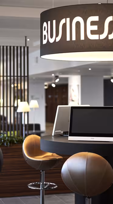 Ein modernes Business Center mit schwarzen Tischen und futuristischen Stühlen. Computer stehen auf runden Tischen, unter großen Schildern mit der Aufschrift „Business Center“. Im Hintergrund befinden sich eine Holztrennwand und modernes Dekor.