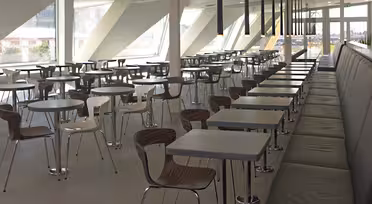 Geräumige, moderne Cafeteria mit Reihen leerer Tische und Stühle. Sonnenlicht strömt durch große Fenster und erhellt den klaren, minimalistischen Innenraum. Eine lange Bank säumt eine Seite des Raumes.