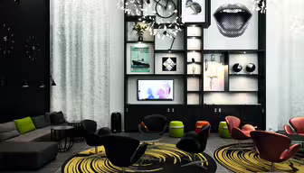 Moderne Lounge mit schwarz-weißer Wandkunst, darunter ein großer Munddruck. Stilvolle Stühle und Teppiche mit kreisförmigen Mustern. Regale bieten Platz für verschiedene Dekoartikel, und im oberen Bereich ist ein Fahrrad montiert. Sanftes Licht sorgt für eine gemütliche Atmosphäre.