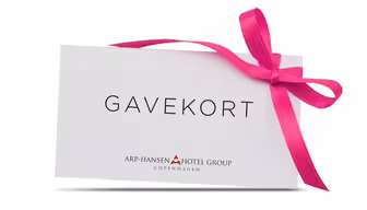 Eine weiße Geschenkkarte mit der Aufschrift „GAVEKORT“ in schwarzer Schrift, geschmückt mit einer leuchtend rosa Schleife auf der rechten Seite. Darunter steht in kleinerer Schrift „Arp-Hansen Hotel Group Copenhagen“.