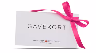 Eine weiße Geschenkkarte mit der Aufschrift „GAVEKORT“ in schwarzer Schrift, geschmückt mit einer leuchtend rosa Schleife auf der rechten Seite. Darunter steht in kleinerer Schrift „Arp-Hansen Hotel Group Copenhagen“.