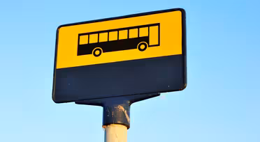 Ein quadratisches gelb-schwarzes Schild mit einem Bussymbol auf einer Stange vor einem klaren blauen Himmel.