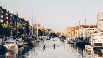 Ein malerischer Kanalblick, gesäumt von Gebäuden und Booten. Das ruhige Wasser spiegelt den klaren blauen Himmel. Menschen fahren mitten auf dem Kanal Kajak und schaffen so eine friedliche und einladende Atmosphäre.