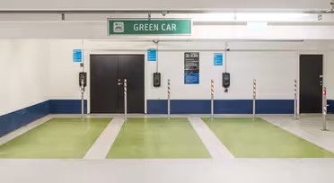 Tiefgarage mit Grünflächen für Elektrofahrzeuge. Über drei leeren Parkplätzen ist ein „GREEN CAR“-Schild zu sehen. Ladestationen sind an der Wand montiert, der Boden ist mit grüner Farbe markiert.